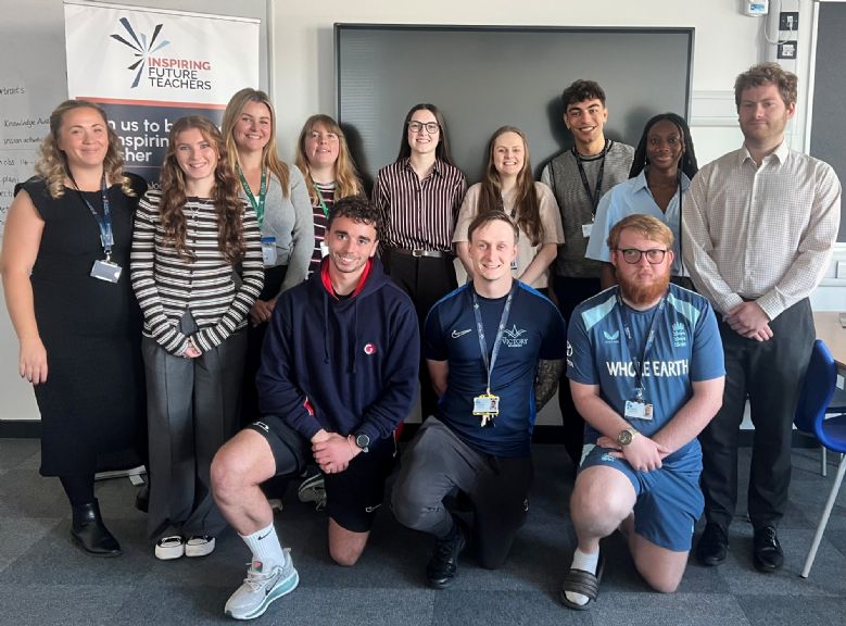 Group of trainee teachers and staff in a classroom beside an Inspiring Future Teachers banner